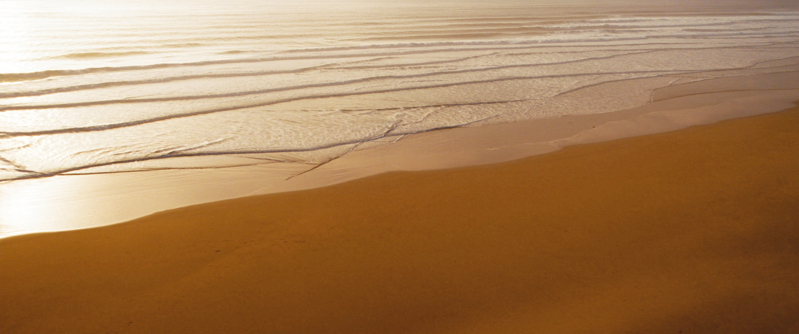 Ocean waves rolling onto a golden beach at sunrise